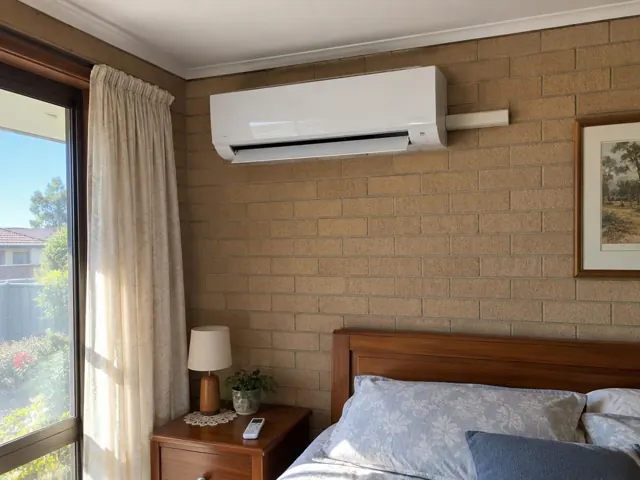 Wall-mounted split system above a bed on a brick wall in a bedroom in Craigmore