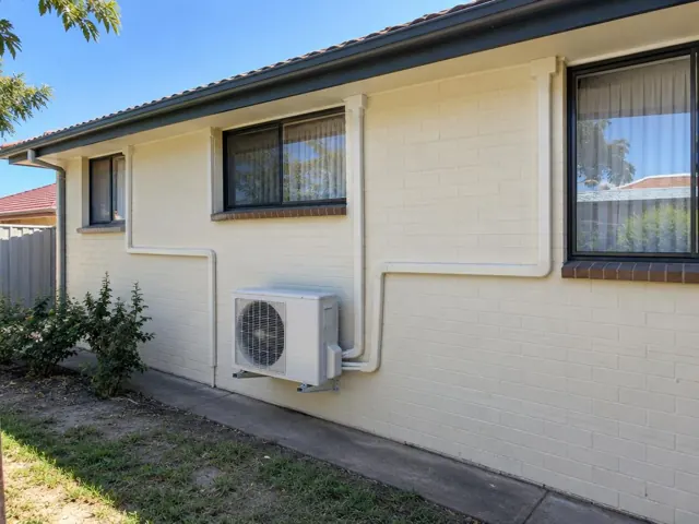 Outdoor air conditioning unit on a brick wall with neat pipe covers on a single-storey home in Craigmore