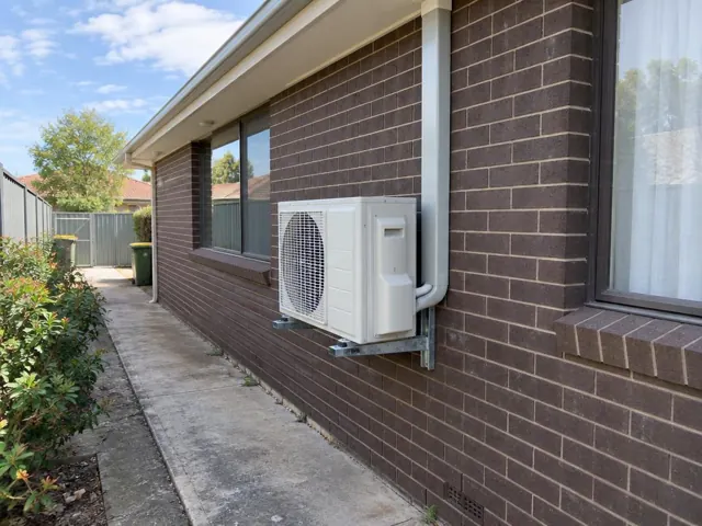 Outdoor air conditioner unit on wall brackets beside a brick house and side path in Elizabeth Downs